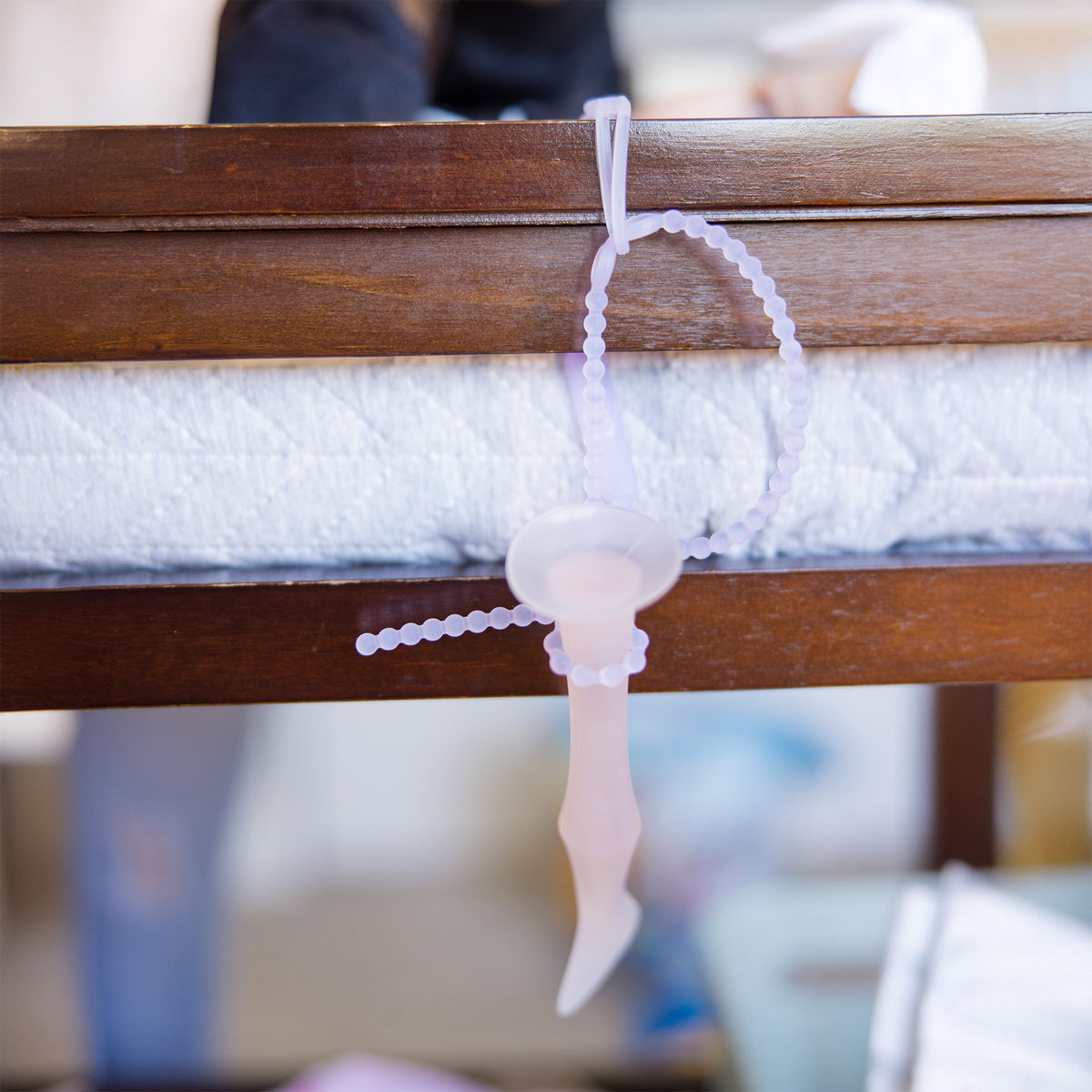 Pink silicone pacifier tether hanging over a wooden crib rail.