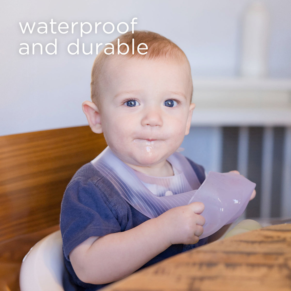 Happy infant sitting in a highchair wearing a durable easy to clean silicone pocket bib during mealtime