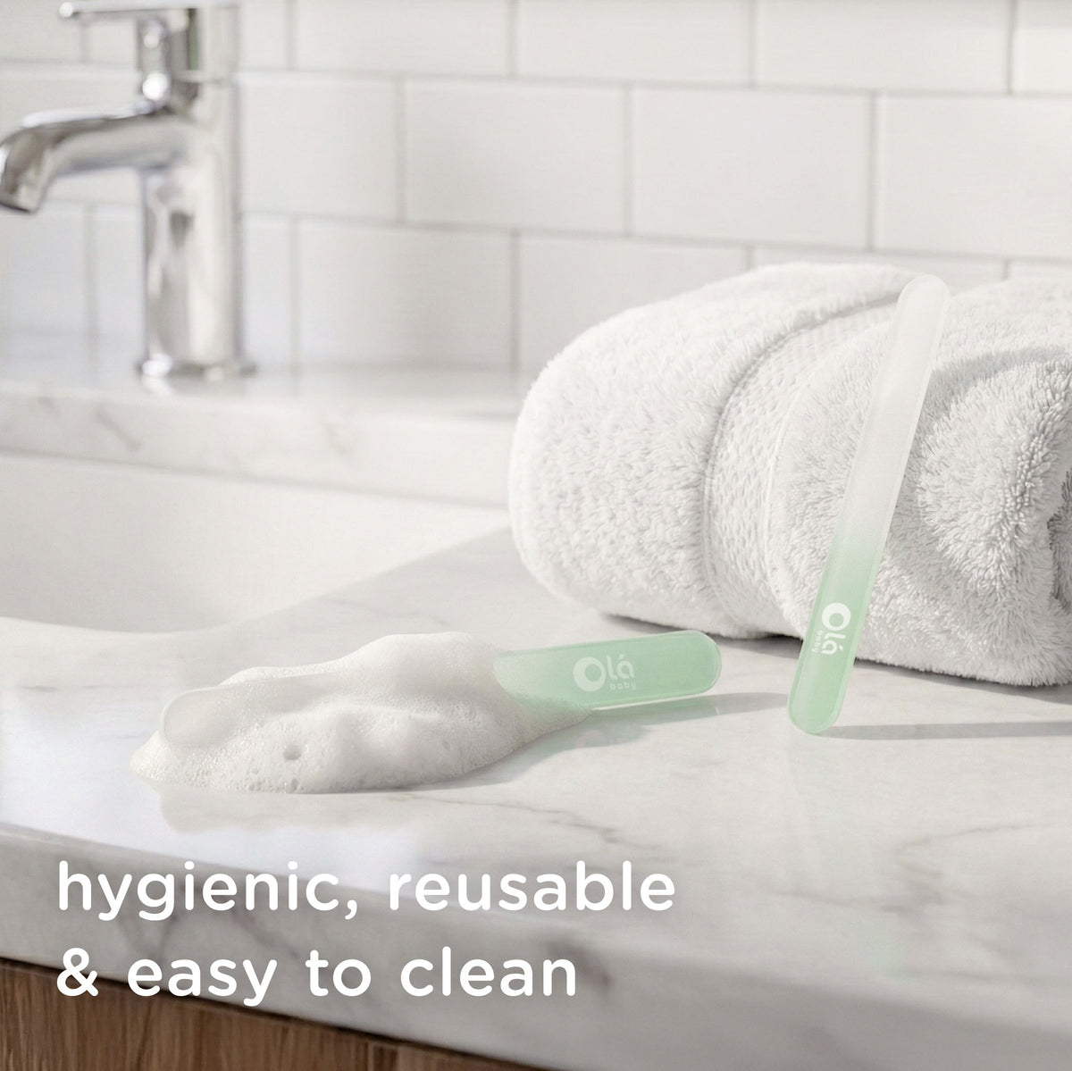 Olababy reusable baby glass nail file on a bathroom counter next to soapy water to demonstrate its hygienic and easy-to-clean design.