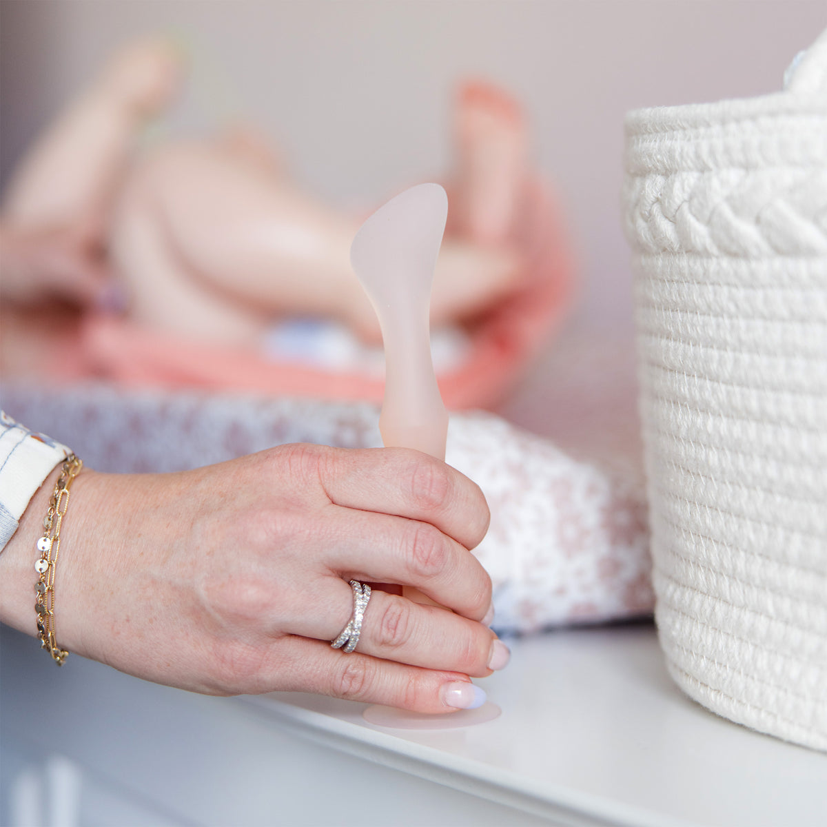 A hand suctioning the coral Olababy diaper rash paste applicator onto a clean surface to prevent product transfer and mess.